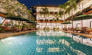 A swimming pool with lounge chairs and umbrellas, surrounded by greenery and a multi-story building with balconies. - The Sears Residence (Siem Reap)