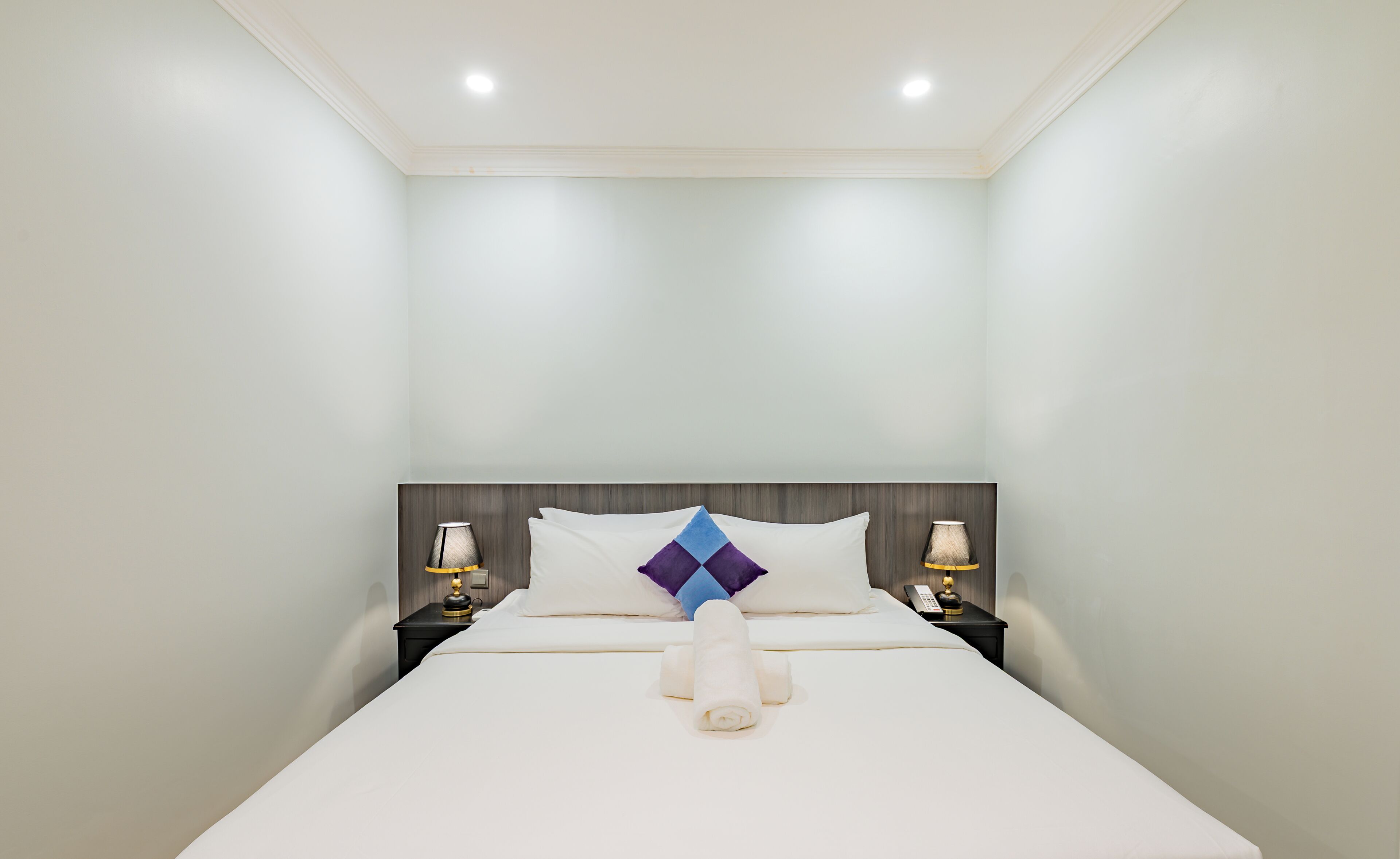 Habitación de hotel con una cama bien tendida, dos mesitas de noche con lámparas y un cabecero moderno.