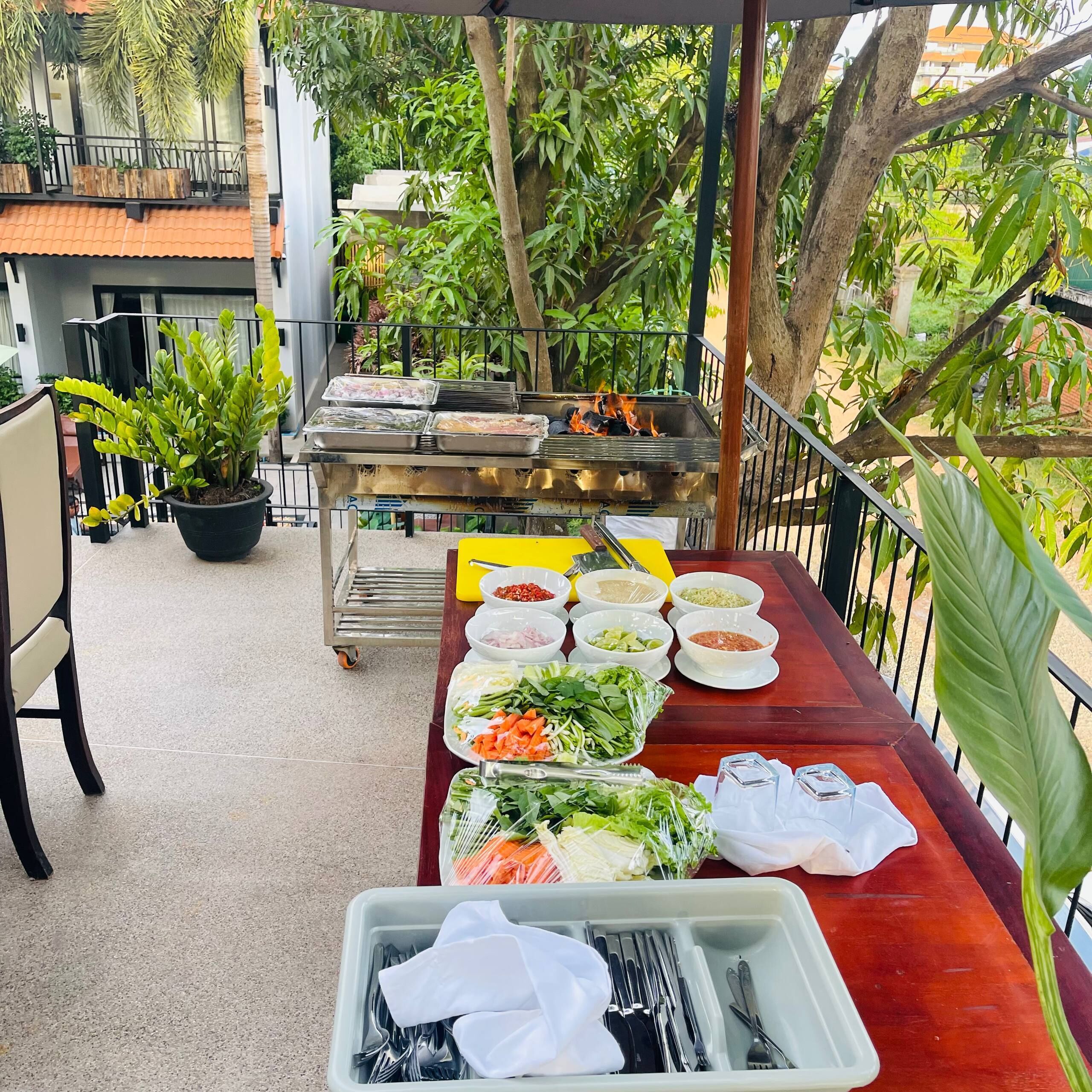 An outdoor dining area with a grill, various food items, and a potted plant.