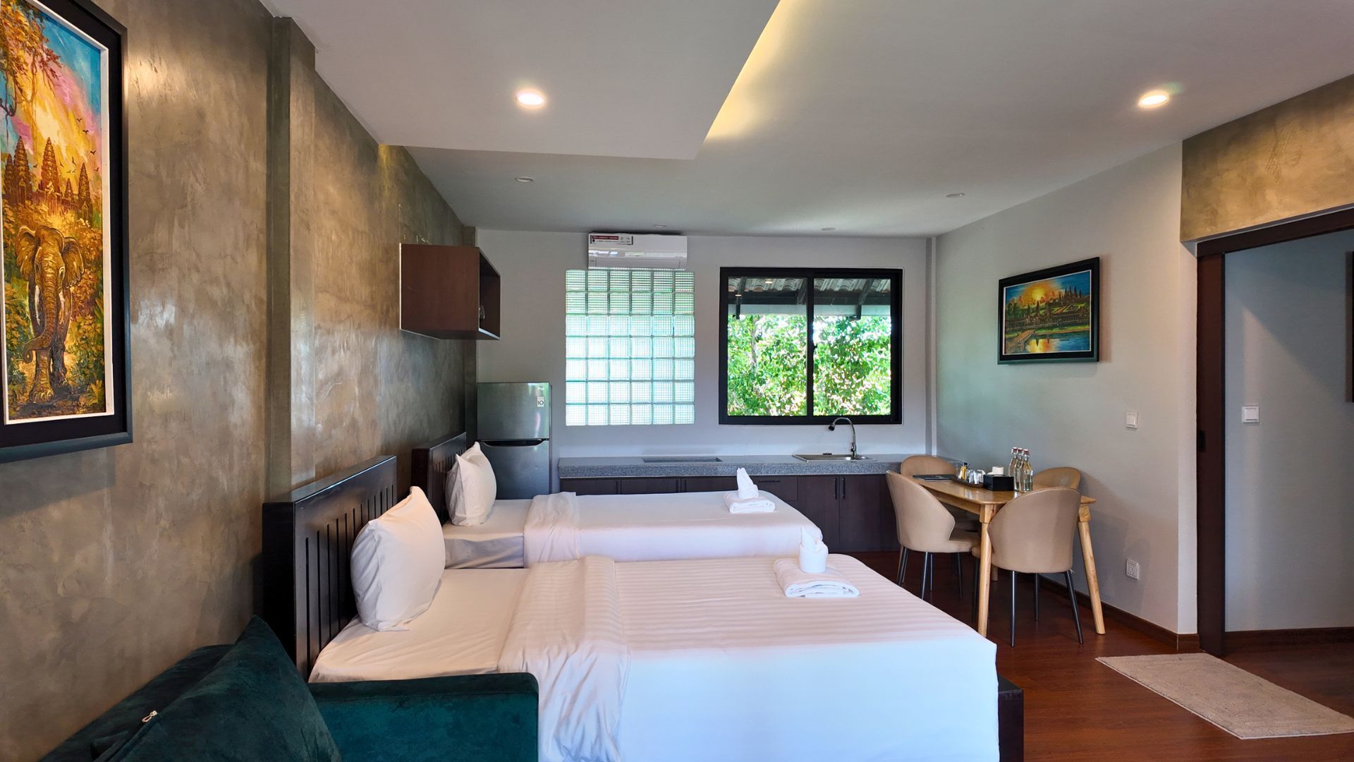 A hotel room with two beds, a desk, a chair, and a window with a view of greenery.