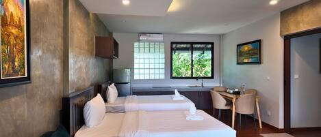 A hotel room with two beds, a desk, a chair, and a window with a view of greenery.