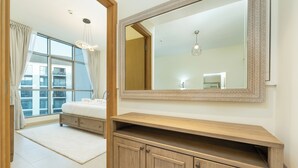 Ein Schlafzimmer mit großem Fenster, einem Bett, einem Schminktisch mit Spiegel und einer Leuchte.