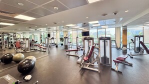 Ein Fitnessstudio mit unterschiedlichen Trainingsgeräten, großen Fenstern und einer Spiegelwand.