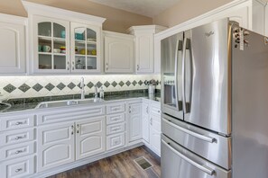 Una cocina con armarios blancos, un refrigerador de acero inoxidable y un salpicadero de azulejos verde y blanco.