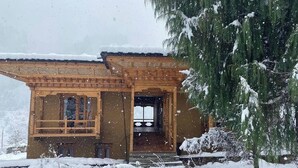 A wooden cabin with a porch and a window, surrounded by snow-covered ground and trees. - Sonam Zhidhey Resort  (Ha)