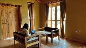 A room with wooden floors, a sofa, a table, and a person using a laptop. - Sonam Zhidhey Resort  (Ha)