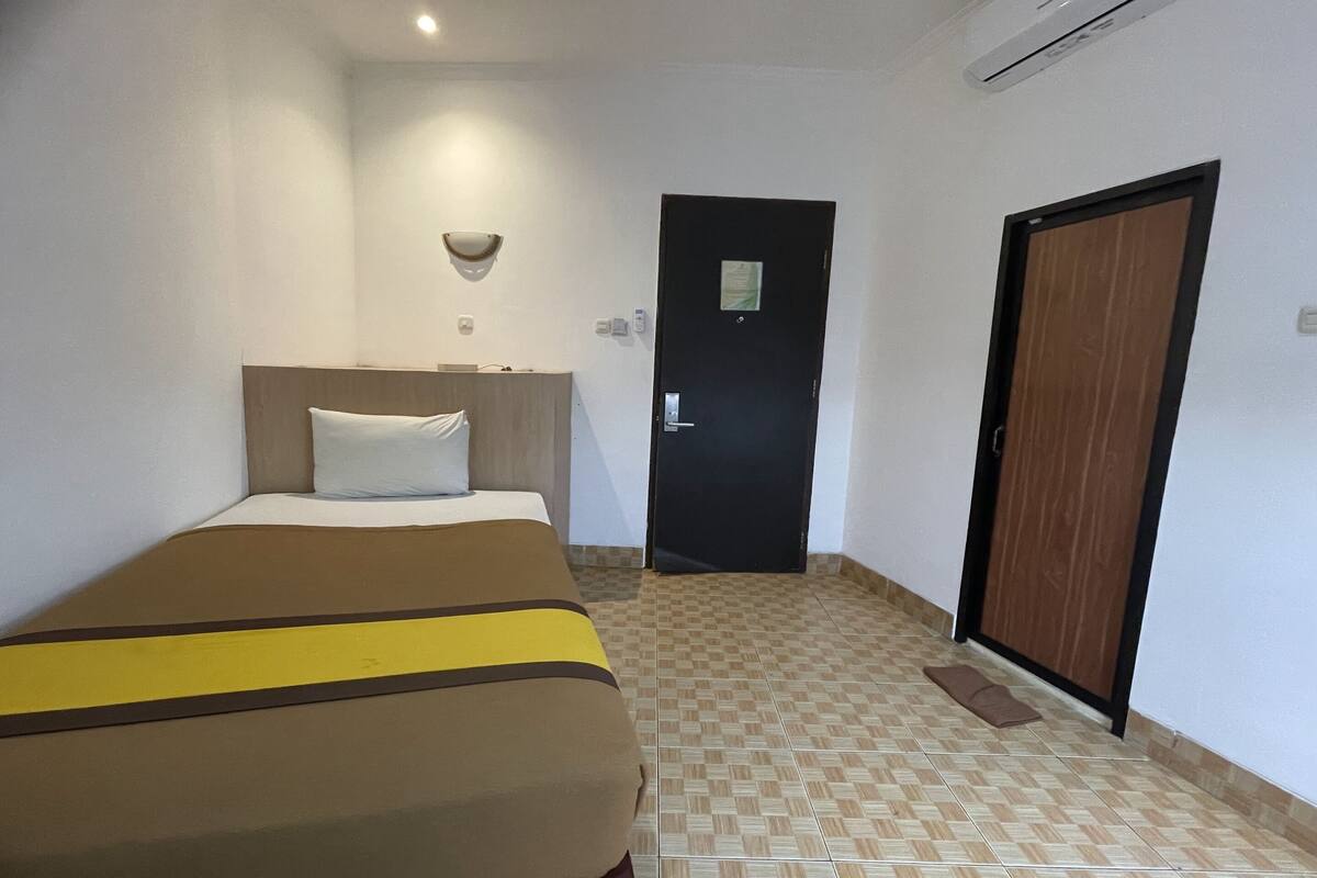 A hotel room with a bed, a door, and a wall-mounted light fixture.