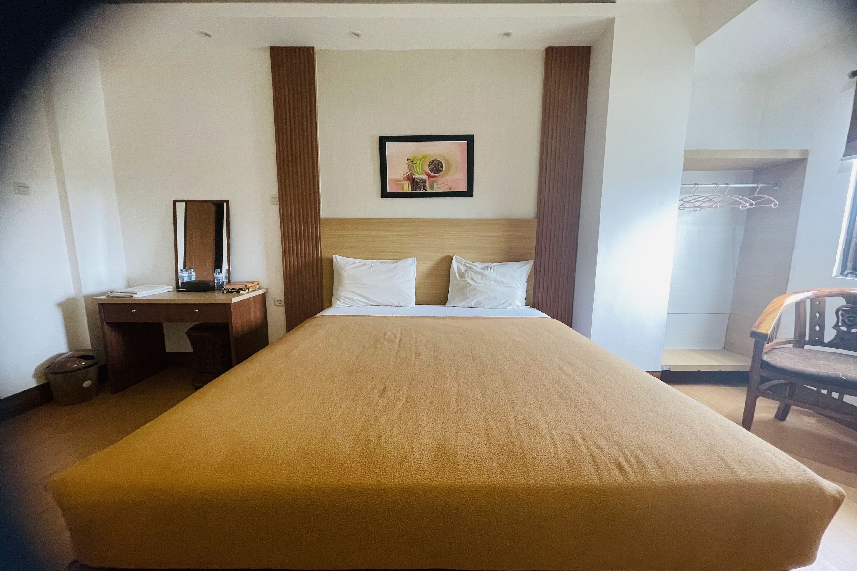 A hotel room with a large bed, a desk with a chair, a wardrobe, and a mirror.