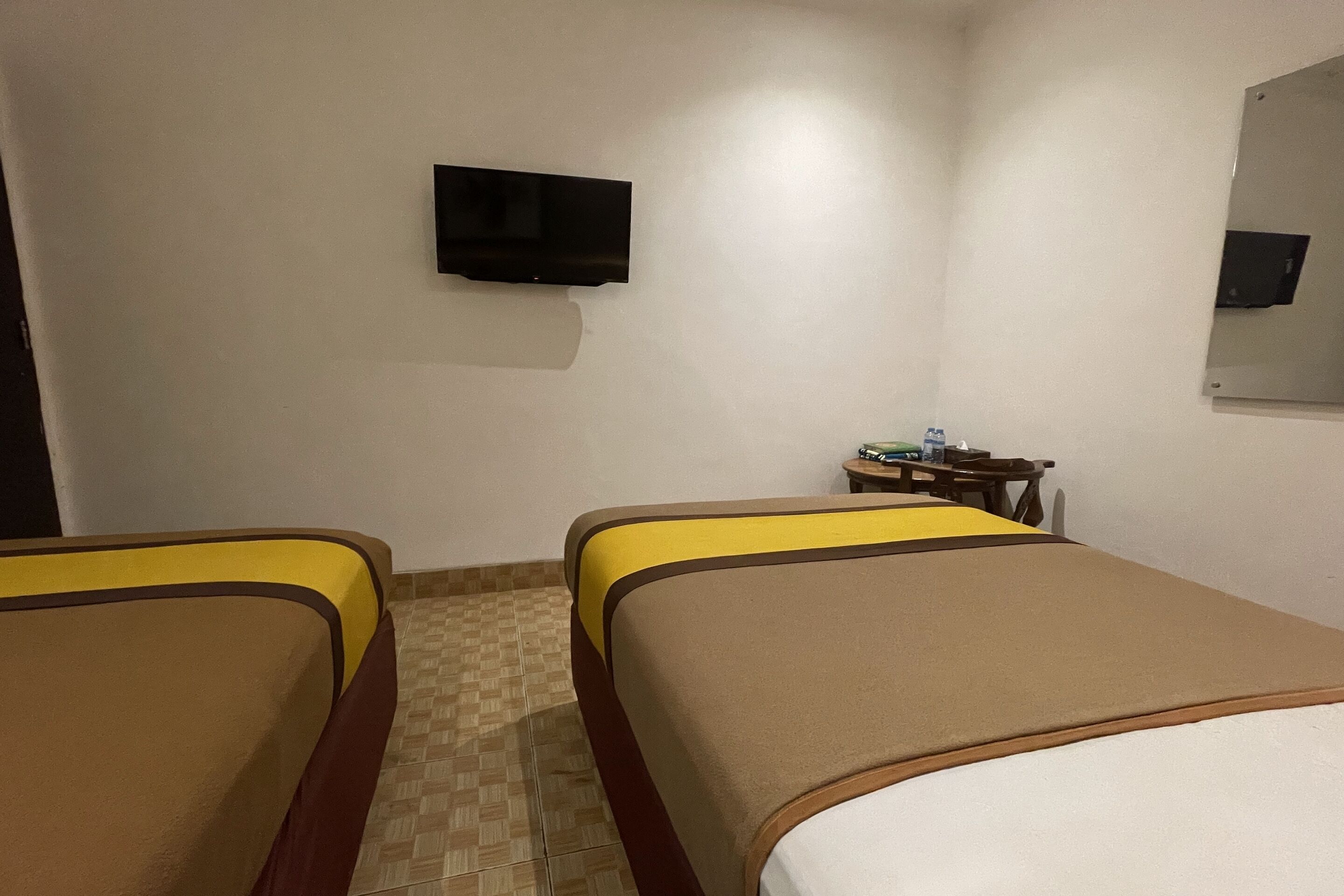 A hotel room with two beds, a television on the wall, and a small table with a chair.