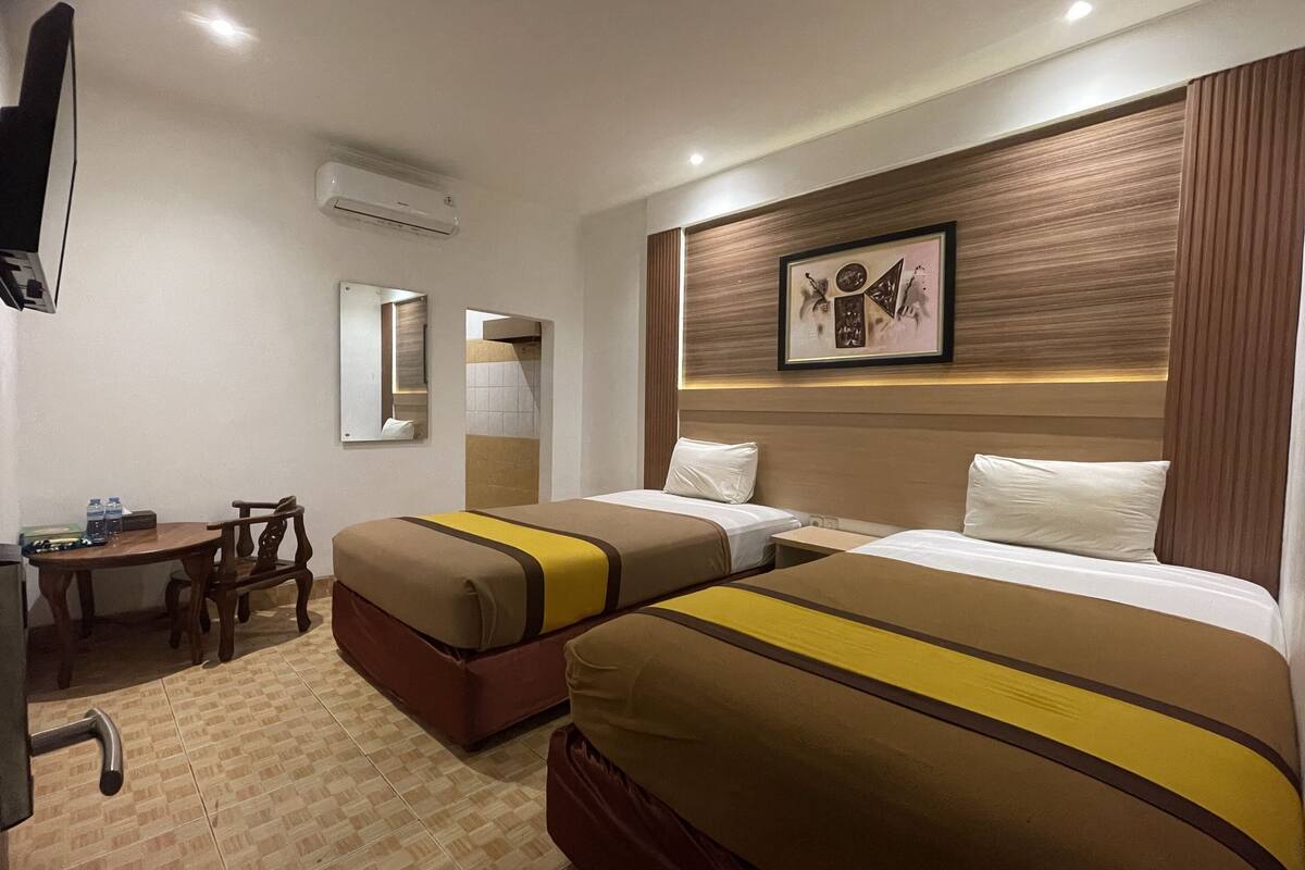A hotel room with two beds, a desk, a chair, a television, and a framed picture on the wall.