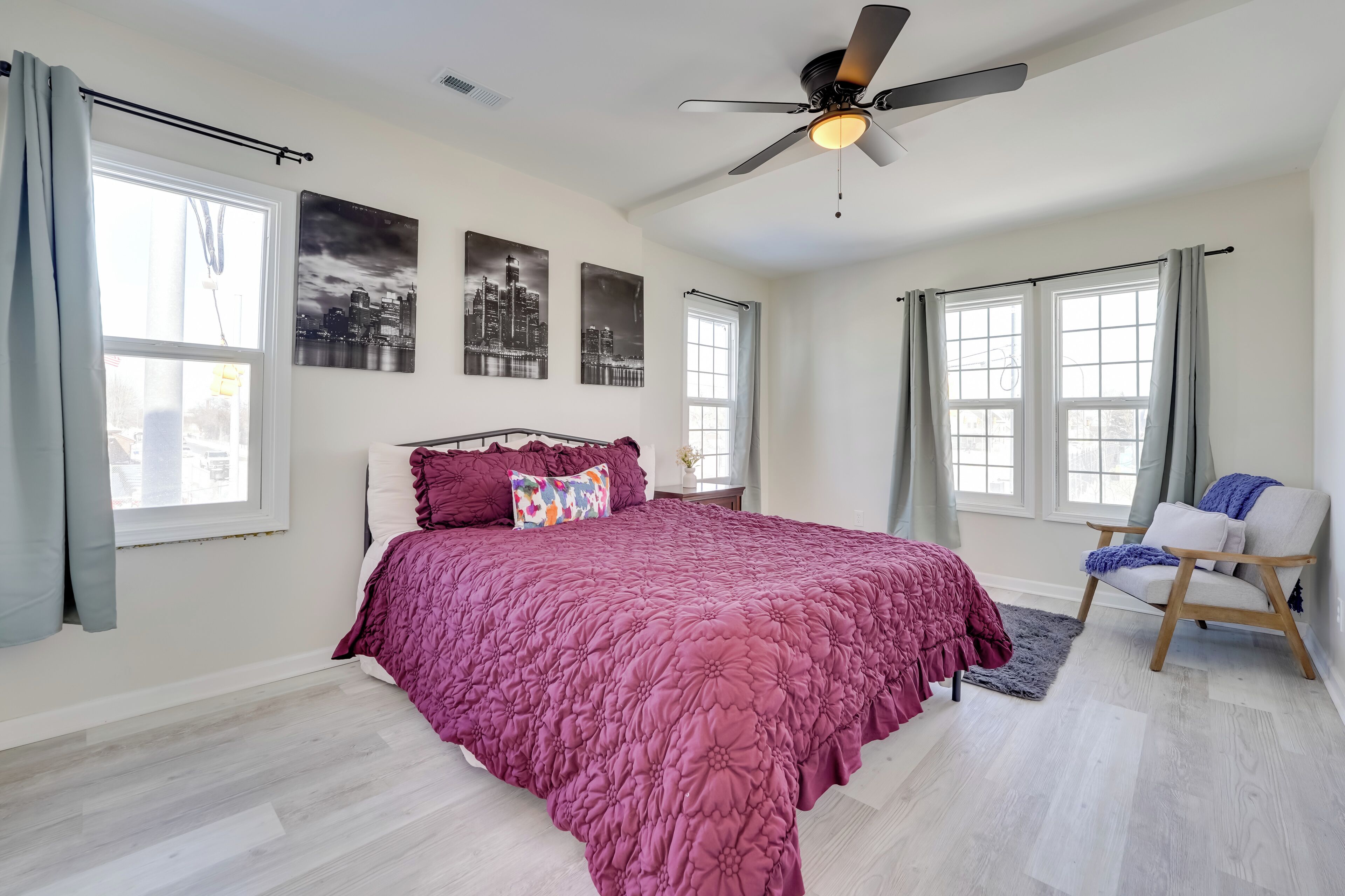 A bedroom with a large bed, a ceiling fan, and two windows with curtains.