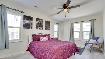 A bedroom with a large bed, a ceiling fan, and two windows with curtains.