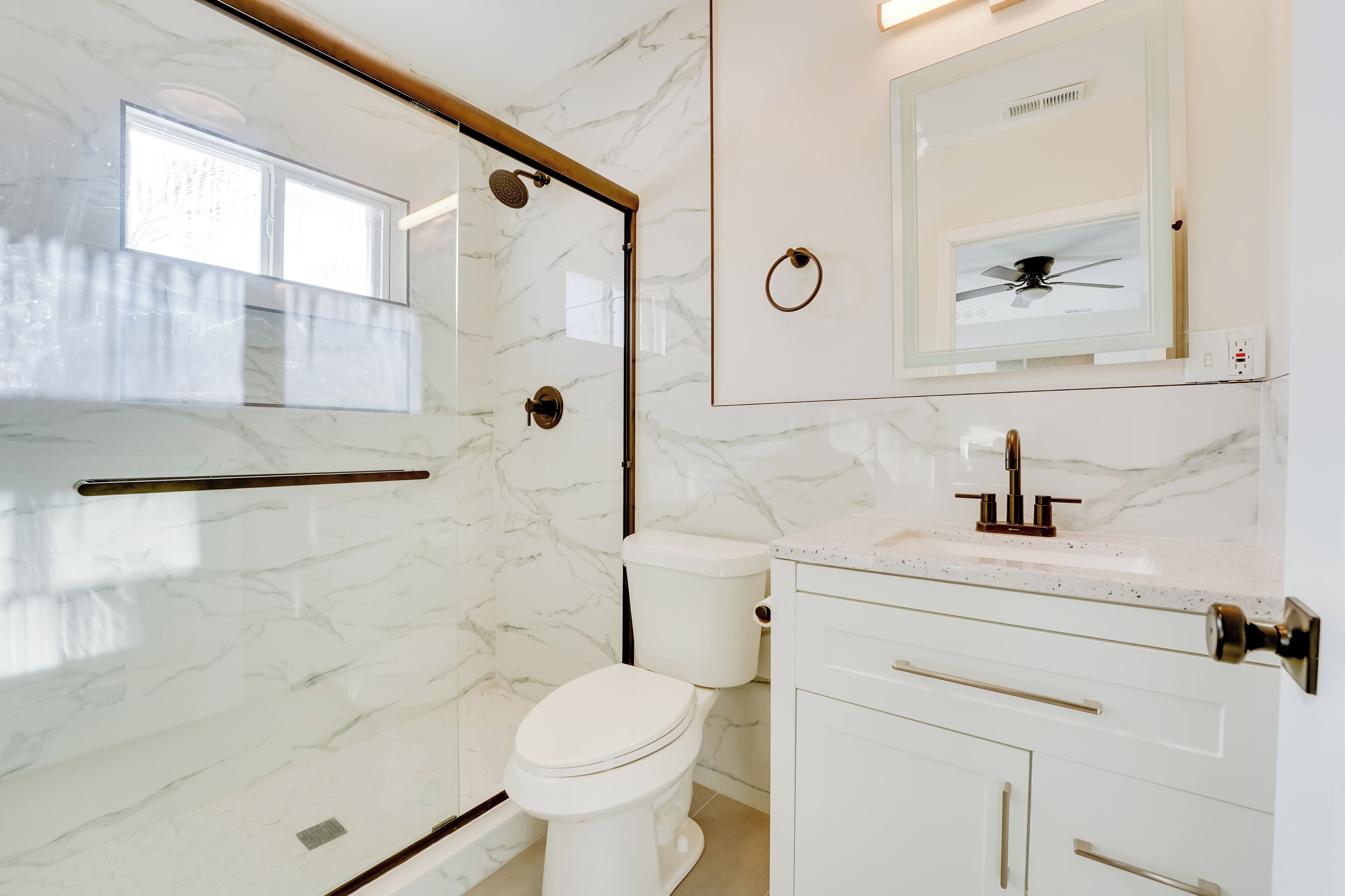 Une salle de bain moderne avec une douche à parois de verre, des toilettes et un meuble-lavabo doté d’un miroir et d’un évier.