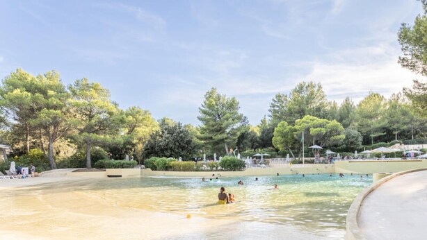 A swimming pool area with clear water, surrounded by trees and shaded by umbrellas. - 2 Room Apartment for 5 People Comfort (Mallemort)
