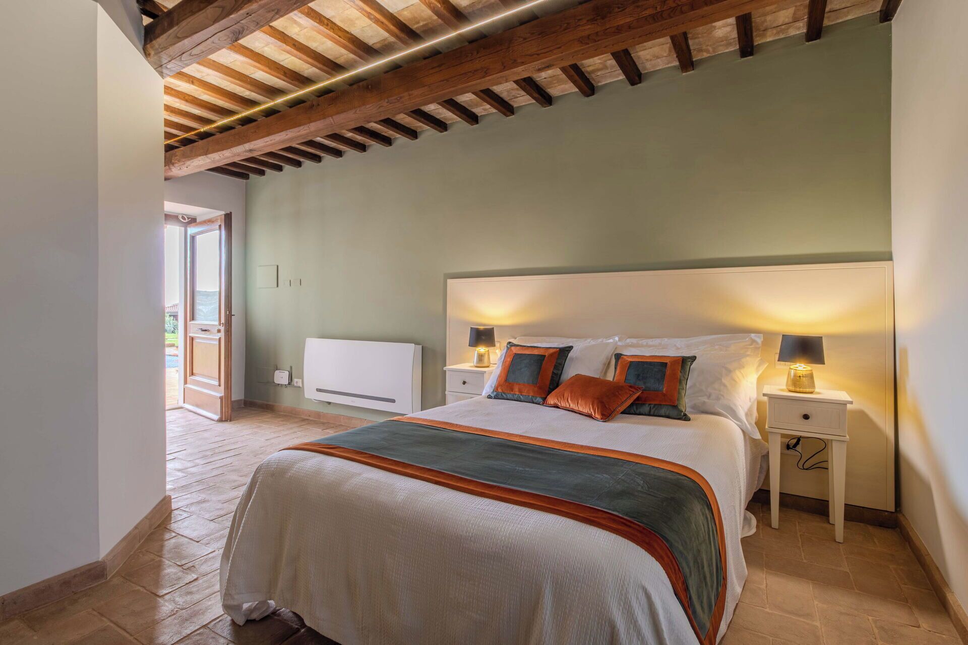 A bedroom with a large bed, wooden ceiling beams, a radiator, and two bedside tables with lamps.