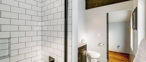 A modern bathroom with white subway tiles, a glass shower enclosure, a wooden floor, and a white toilet.