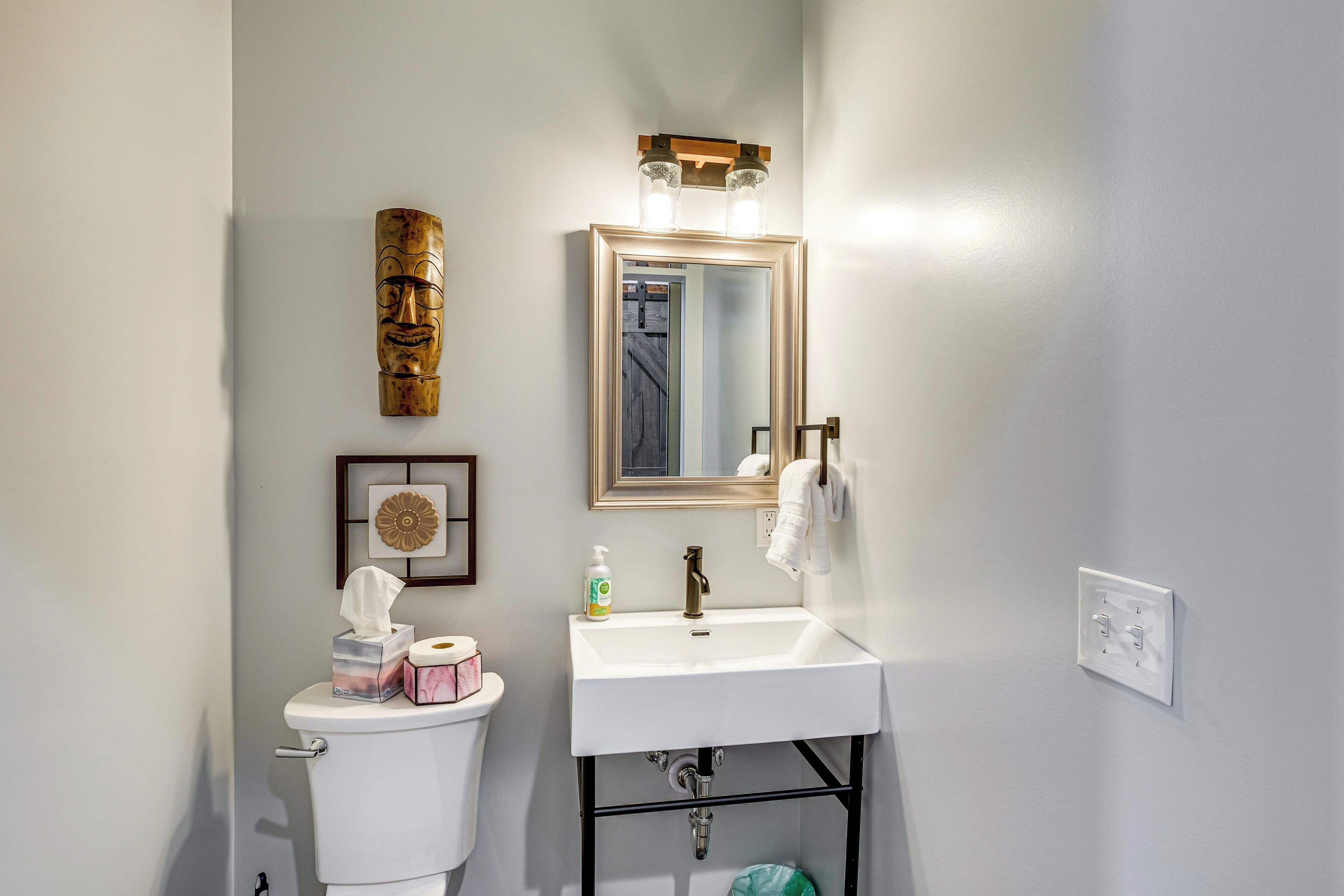 A bathroom with a white sink, a mirror, a toilet, and a decorative wall piece.