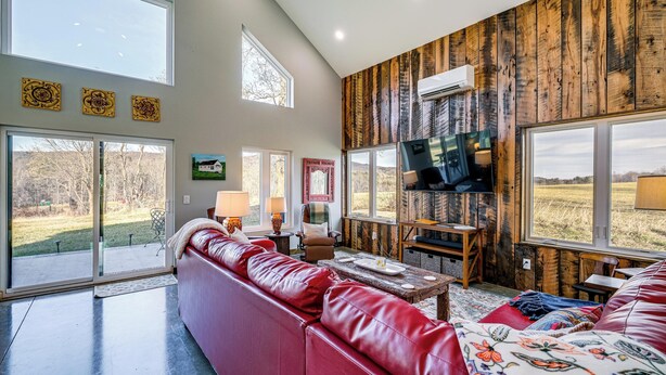 Amplia sala de estar con un sofá de cuero rojo, un televisor montado en una pared de madera y ventanas grandes con vistas al exterior.