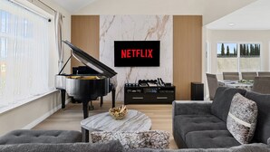 A modern living room with a grand piano, a flat-screen TV displaying 'NETFLIX', a comfortable sofa, and a coffee table. - Relax & Unwind: Pool, Jacuzzi & Private Backyard (Rowland Heights)