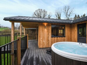 Una cabaña de madera con jacuzzi, terraza cubierta y pared de piedra.