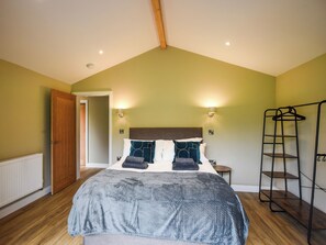 Een slaapkamer met een schuine kap, een bed met een grijze deken, twee wandlampen, een houten deur en een metalen plankunit.
