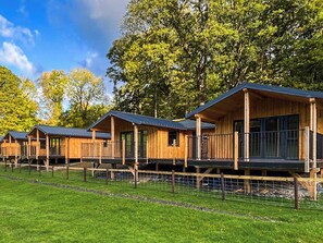 Une rangée de cabanes en bois dotées de balcons, entourées d’une zone herbeuse et d’arbres.