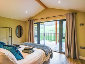 Une chambre à coucher avec un lit, un miroir, une fenêtre avec des rideaux et une vue sur un paysage verdoyant.