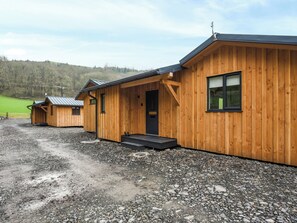 Una hilera de cabañas de madera con un camino de grava y una colina boscosa al fondo.