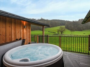 Une cabane en bois avec un jacuzzi et une vue sur un champ verdoyant.