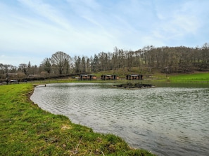 A serene lakeside setting with a row of wooden cabins, a grassy bank, and a forested backdrop.