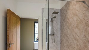 Un baño moderno con cabina de ducha de vidrio, una puerta de madera y vistas a una habitación con ventana.