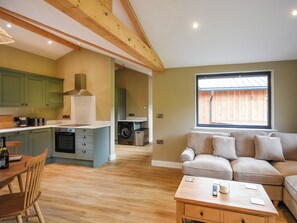 A modern kitchen with wooden beams, a dining area with a table and chairs, a sofa, and a window with a view. - Oakwood Lodge - UK50626 (Welshpool)