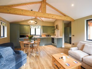 Een ruime woonkamer met een houten plafond, een eettafel met stoelen, een bank en een keuken met groene kastjes.