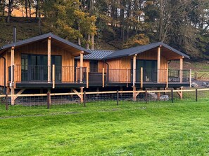 Een houten chalet met balkon, omringd door een omheinde tuin en bomen.