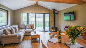 A cozy living room with a sofa, a wooden coffee table, a fireplace, and a dining area with a table and chairs. - Lakeside Lodge - UK50627 (Welshpool)