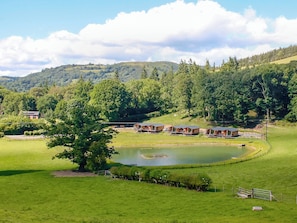 Un paisaje rural con un estanque, campos verdes y una hilera de cabañas de madera.