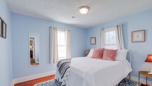 Quarto com cama, espelho, janela com cortinas, mesa de cabeceira e abajur.