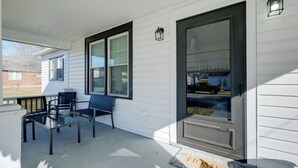 Een overdekt terras met een glazen tafel en stoelen, een deur met deurmat en een raam met zonwering.