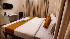 Hotellihuone, jossa on sänky, työpöytä, tuoli, televisio ja verhot.