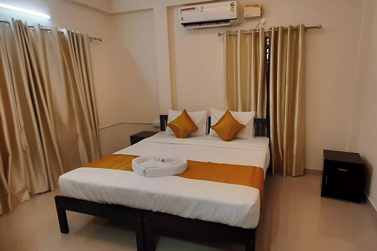 Una habitación de hotel con cama, cortinas, un equipo de aire acondicionado y un cuadro en la pared.