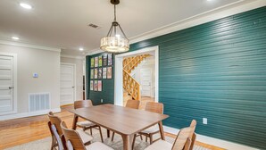 Uma sala de jantar com mesa e cadeiras de madeira, um lustre e uma parede cor de verde-água.