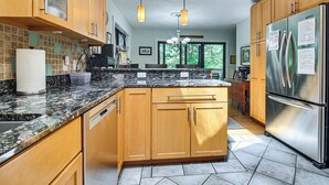 Una cocina con armarios de madera, un refrigerador de acero inoxidable, encimeras de granito e iluminación colgante.