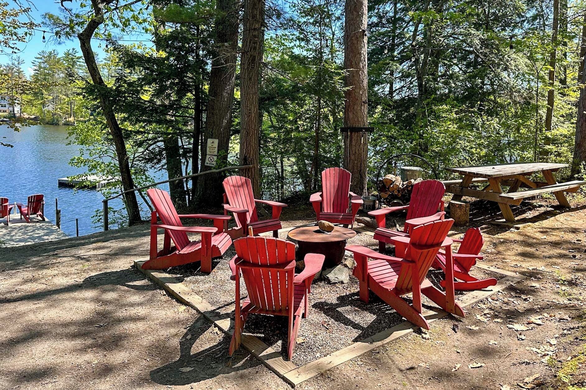 En campingplads ved søen med røde Adirondack-stole, et picnicbord og en dok.
