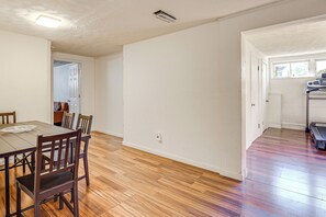 Un comedor con mesa y sillas de madera, una cocina con refrigerador, y un pasillo con puerta que da a otra habitación.