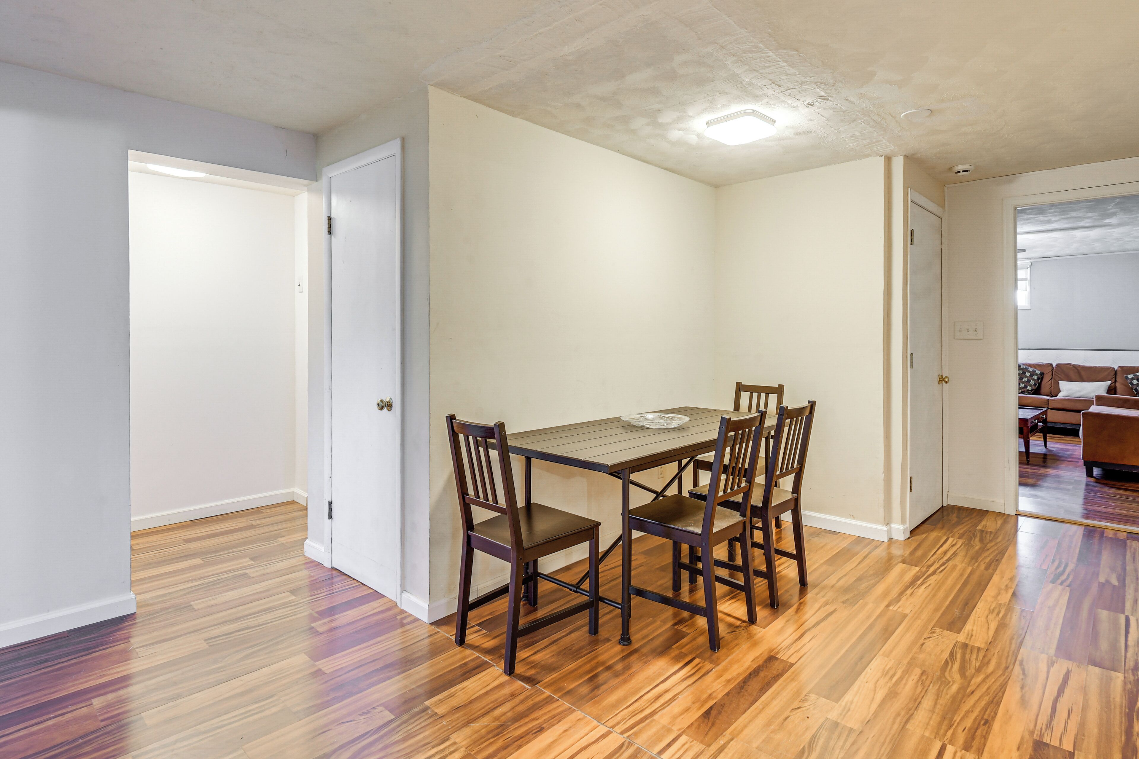 Un comedor con una mesa de madera y cuatro sillas, una puerta blanca y piso de madera.