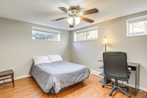 Un dormitorio con una cama, un escritorio, una silla, un ventilador de techo y dos ventanas.