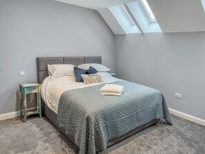 A bedroom with a bed, a nightstand, a skylight, and a carpeted floor.