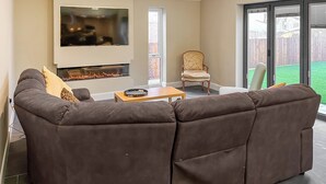 Una sala de estar con un sofá modular, un televisor de pantalla plana, una chimenea y un ventanal corredizo que da a un jardín trasero.
