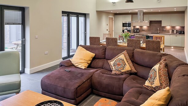 Una sala moderna con sofá modular, comedor, cocina y grandes puertas correderas de vidrio.