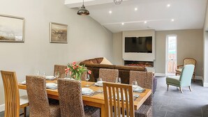 Un comedor con una mesa de madera, sillas de mimbre y un televisor de pantalla plana montado en la pared.